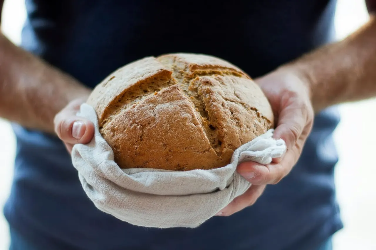 A baker's hands holding a fresh loaf of bread wrapped in linen